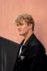 Portrait of a young caucasian male with curly blond hair leaning against a wall in Copenhagen.